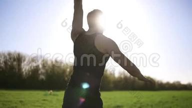 一个穿着黑色T恤的男人正在绿色的草地上做运动.. 用一只手举起重物，把它放在上面